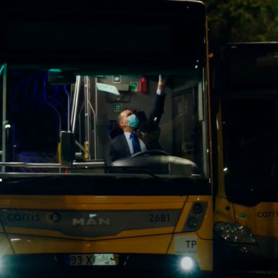 Fotografia de autocarro parado no parque da CARRIS, de noite. No interior, um motorista sentado no banco de condução tem o braço levantado e programa a bandeira de destino